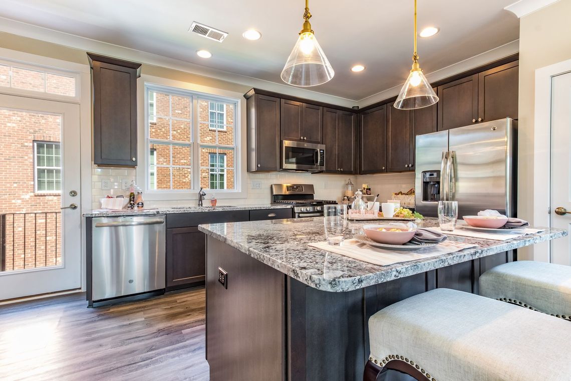 Modern kitchen with dark cabinets, granite island, stainless steel appliances, and two pendant lights.