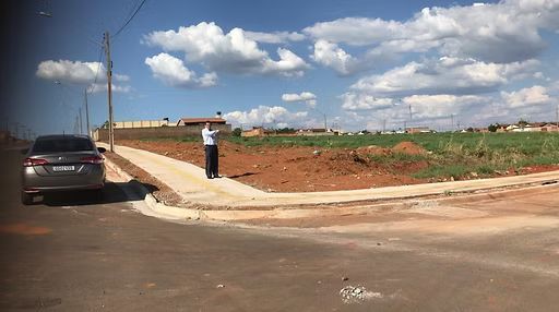 Man taking photo of vacant lot next to a road with a car on a sunny day.