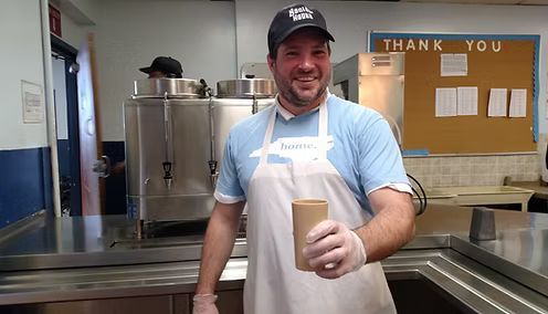 Man in apron holding a cup, smiling in a kitchen.