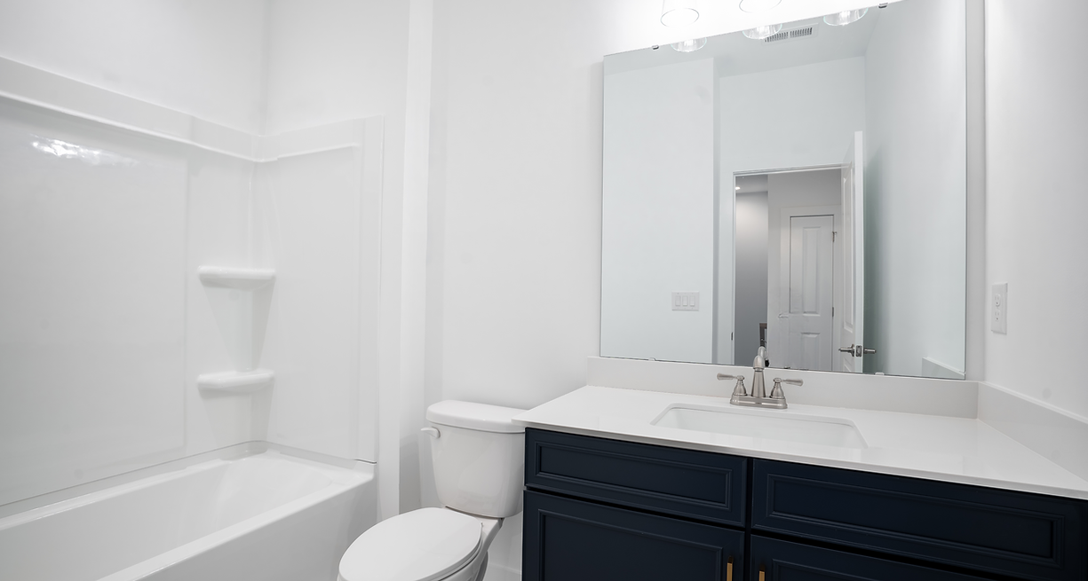 White bathroom with blue vanity, tub/shower combo, and large mirror.