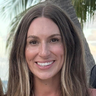Woman with long brown hair smiling outdoors.