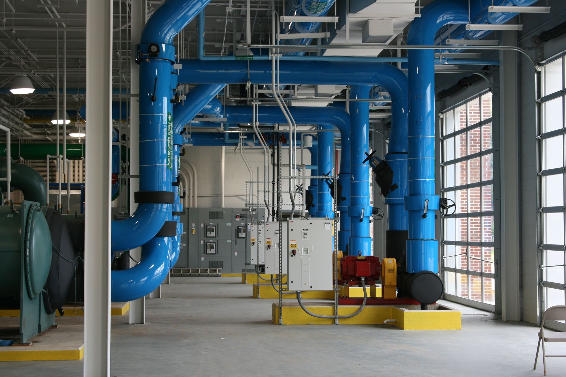 Industrial equipment room with large blue pipes, valves, and machinery in a bright facility