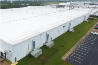 Aerial view of a large white warehouse beside a parking lot and grassy strip