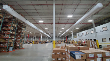 Warehouse aisle with stacked boxes, tall shelving, and overhead lights in a large distribution center