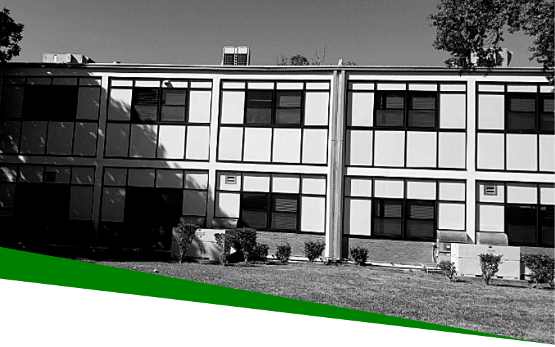 Two-story office building with large windows, trees, and a green lawn in front