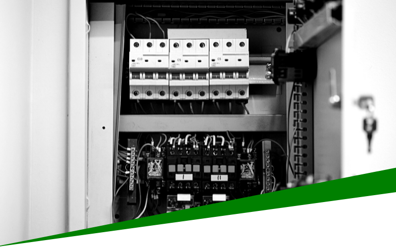 Open electrical control panel with circuit breakers and wiring, partly covered by a green diagonal strip