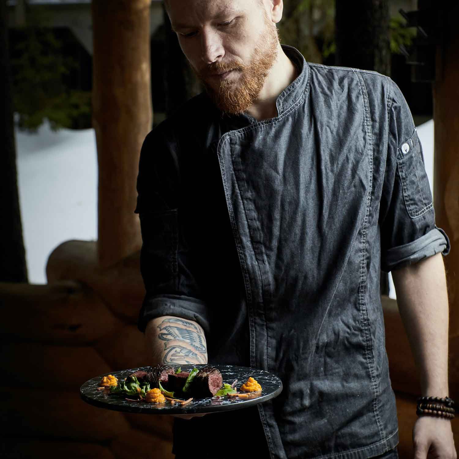 A private chef with a beard is holding a plate of food