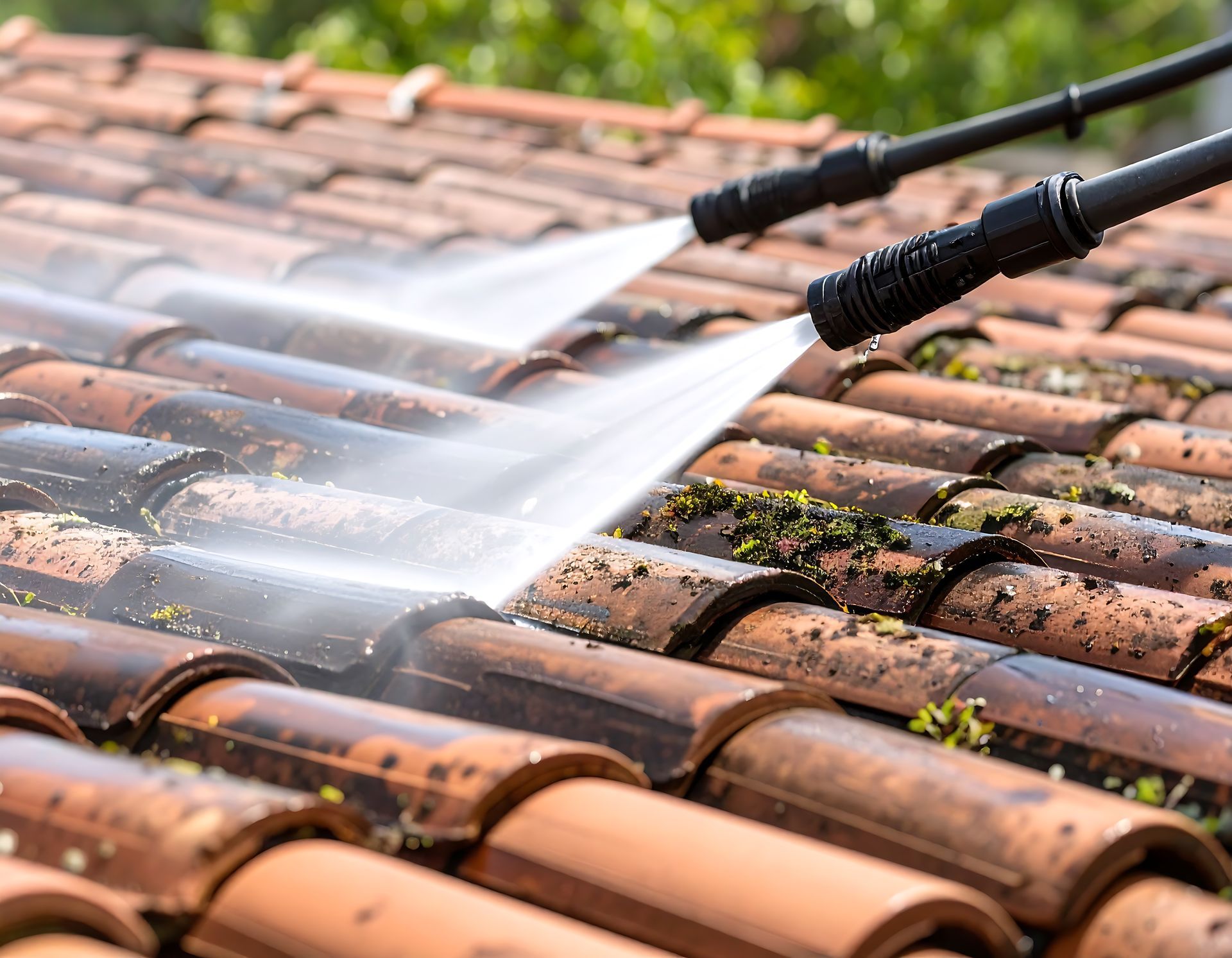 Pressure washers cleaning moss and dirt from a red tile roof.