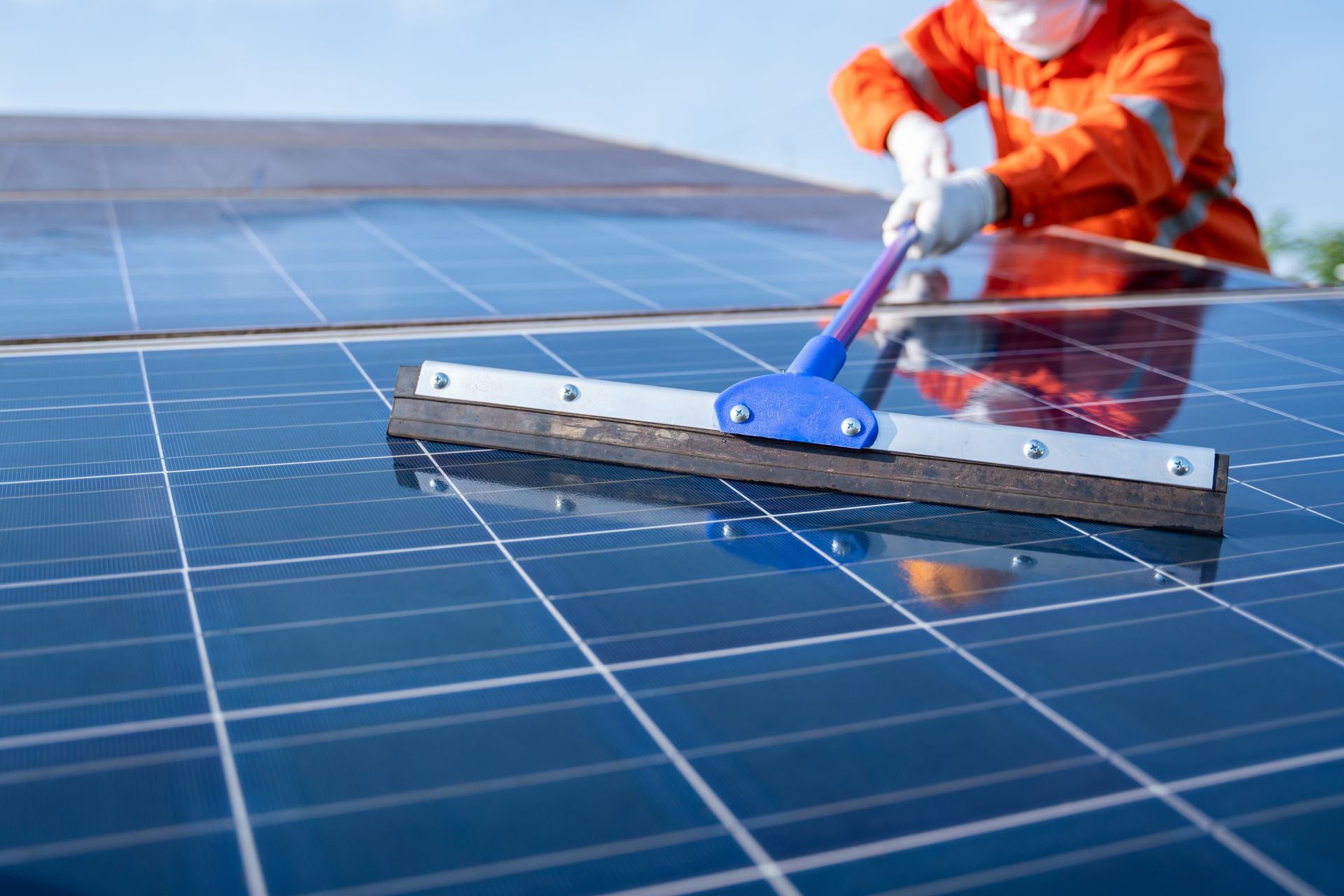 Person cleaning solar panels with a squeegee on a rooftop.