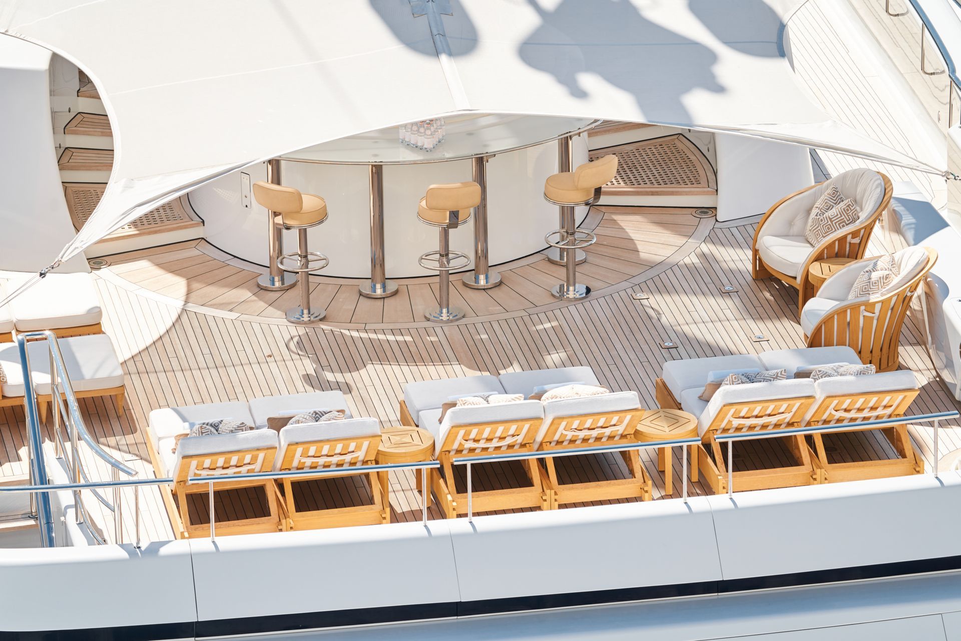 Luxury yacht deck with bar stools, lounge chairs, and sun shade.