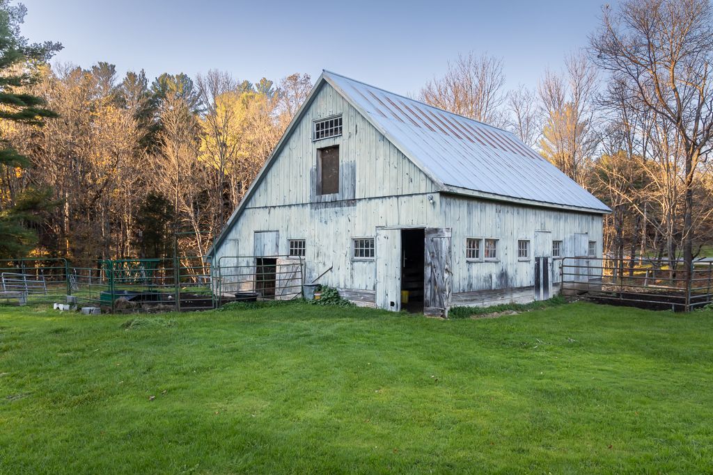 A white barn with a metal roof sits in a grassy field