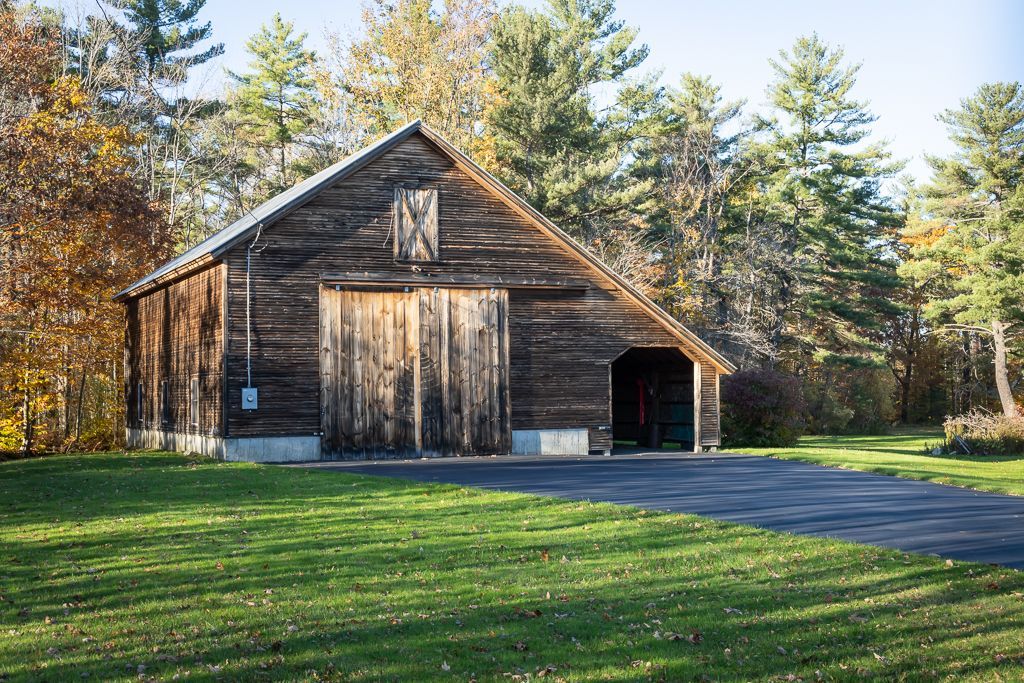 A large wooden barn sits in the middle of a lush green field
