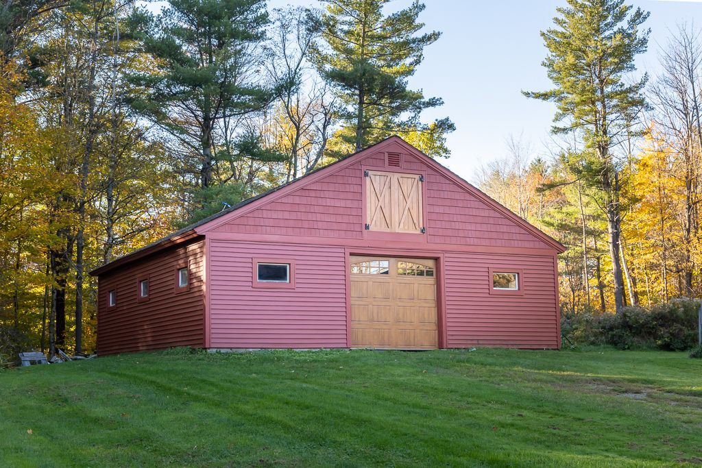 A red barn with a wooden door is surrounded by trees