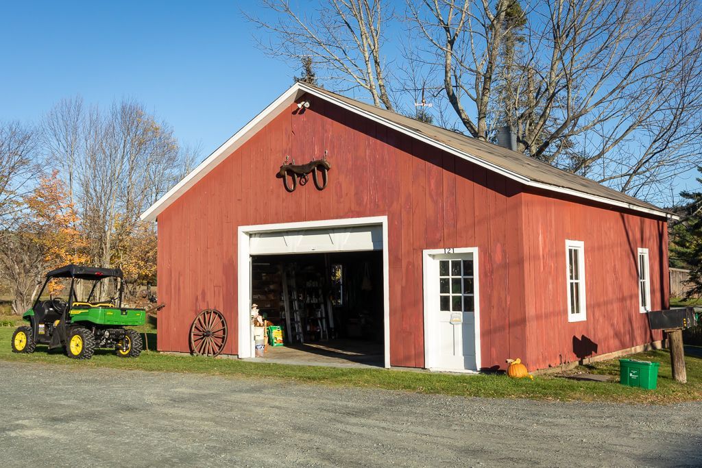 A green tractor is parked in front of a red barn