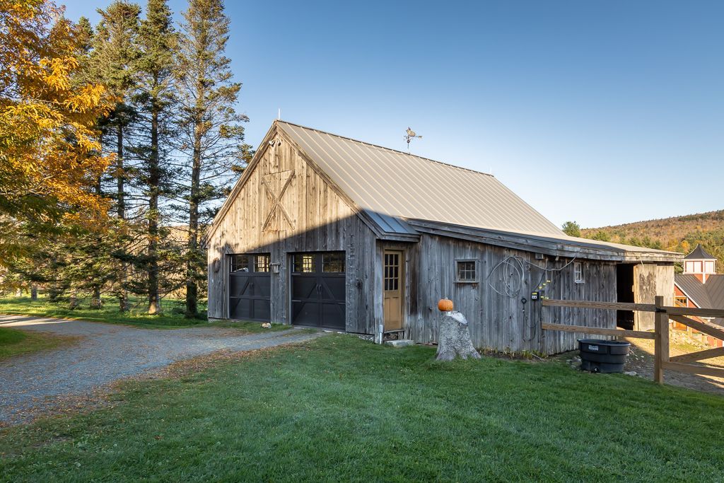 A barn with a metal roof sits in the middle of a grassy field
