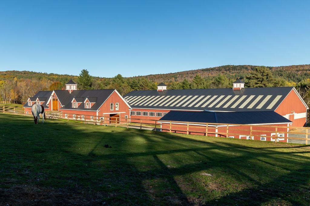 Two horses are walking in front of a large red barn
