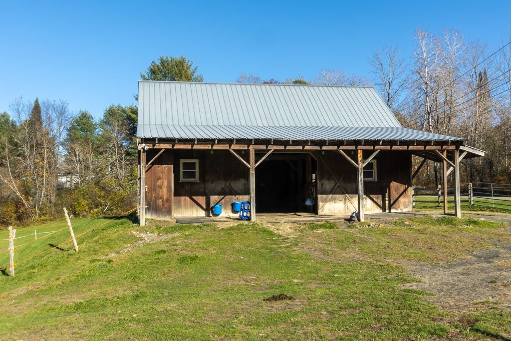 A barn with a metal roof sits in the middle of a grassy field