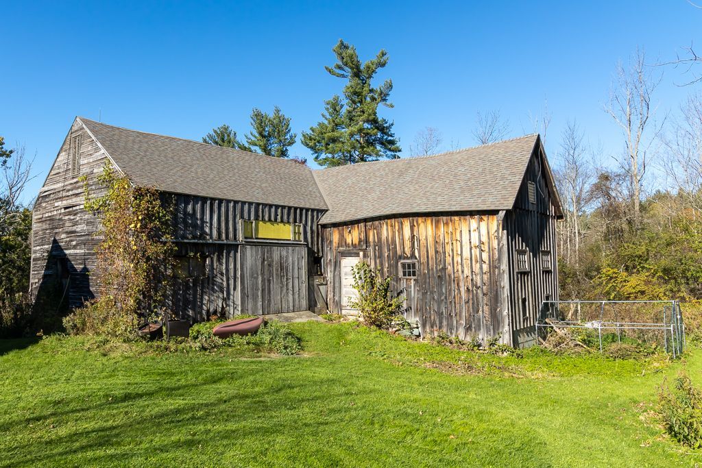 An old barn with a gray roof sits in the middle of a lush green field