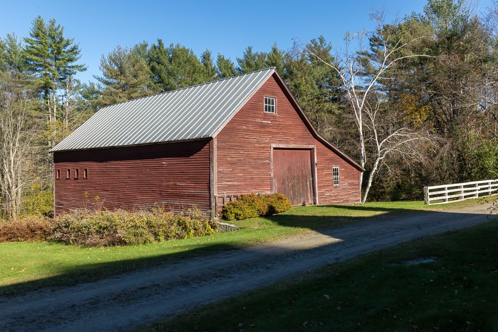 A red barn with a metal roof sits in the middle of a grassy field