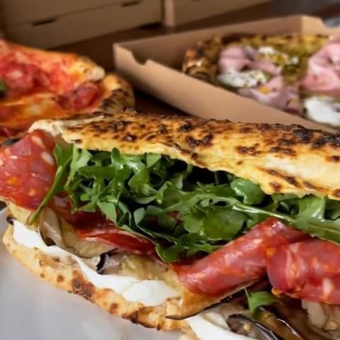 Un panino gourmet preparato con focaccia artigianale, farcito con salame, mozzarella e rucola fresca, con pizze a disposizione.