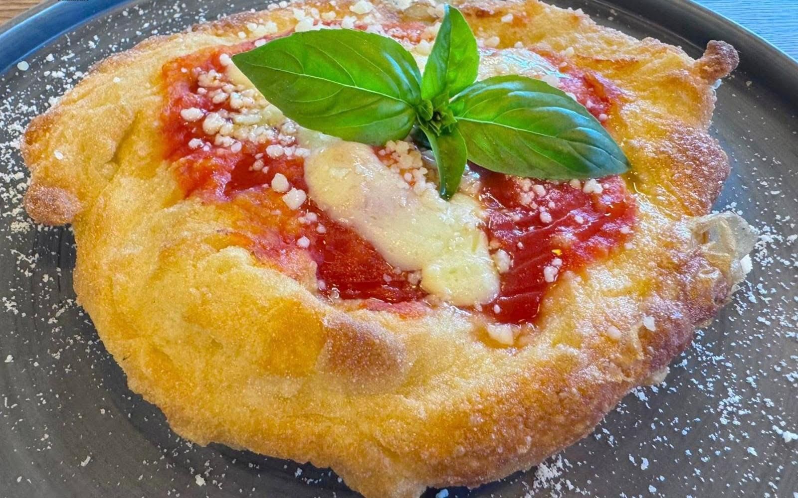Una base per pizza dorata e fritta, condita con salsa di pomodoro, formaggio fuso, parmigiano grattugiato e guarnita con basilico fresco.