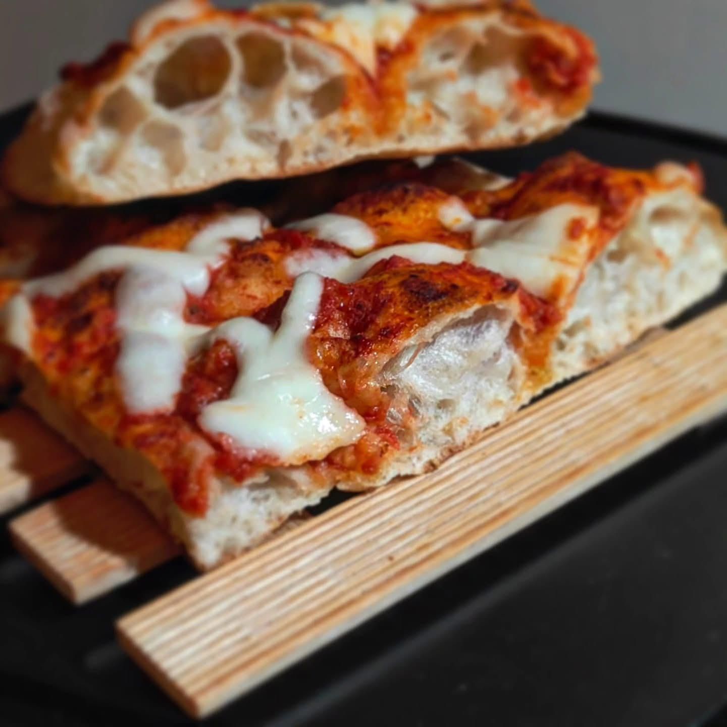 Due fette di pizza al formaggio con una crosta soffice e croccante, adagiate su listelli di legno.