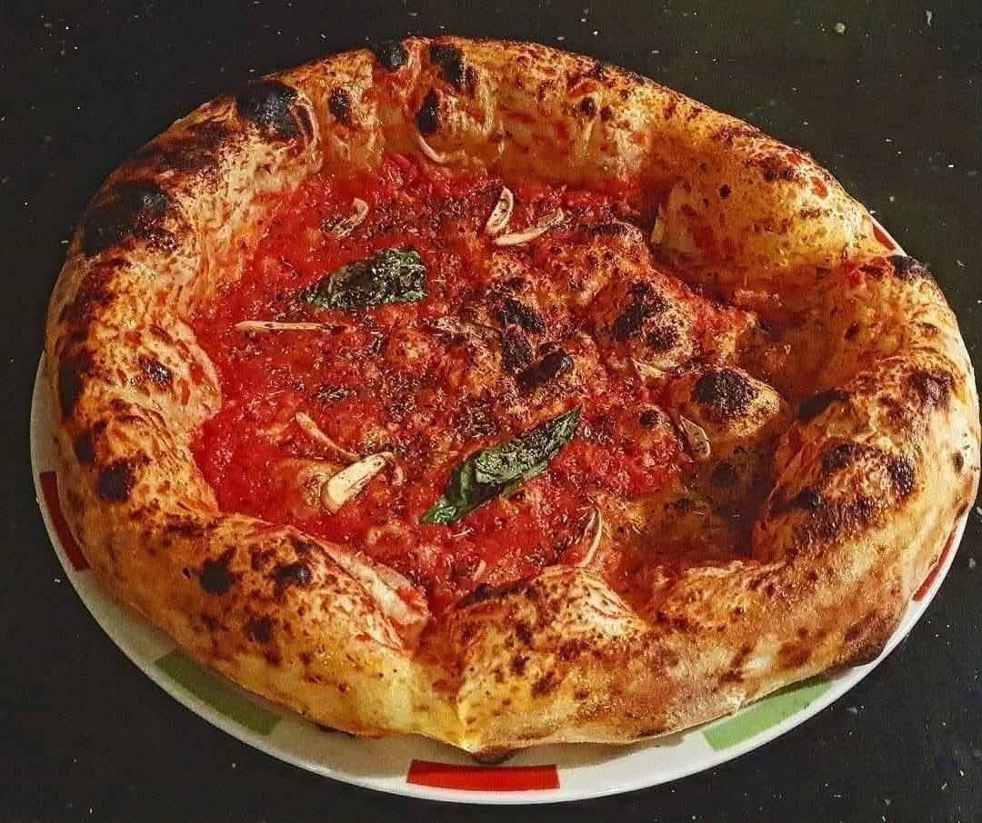Una pizza rustica con una crosta spessa e leggermente bruciacchiata, condita con una salsa di pomodoro vivace, foglie di basilico fresco e aglio tritato.