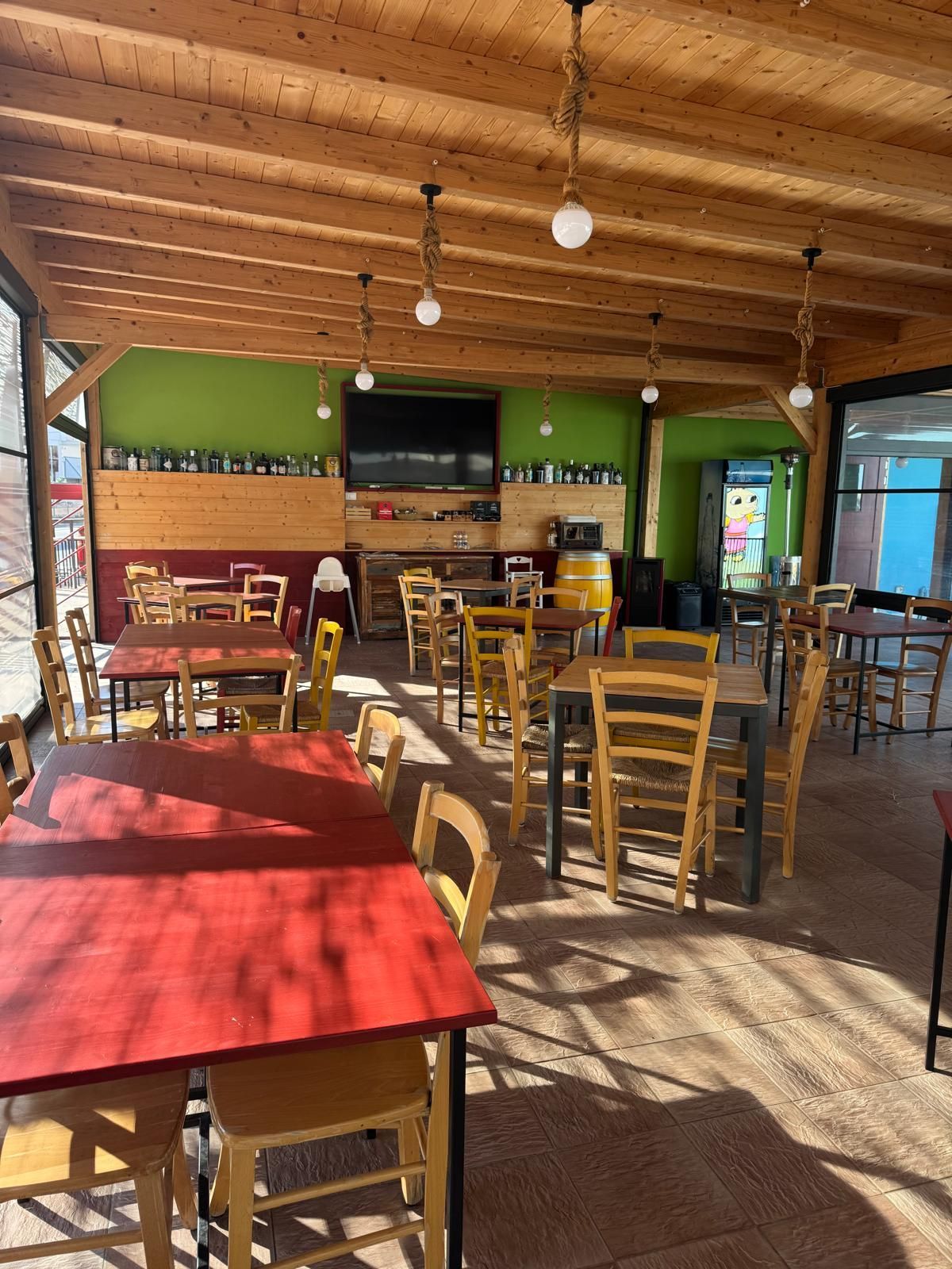 Una zona pranzo esterna coperta con pareti verde brillante, travi in ​​legno a vista, lampade a sospensione e diversi tavoli.