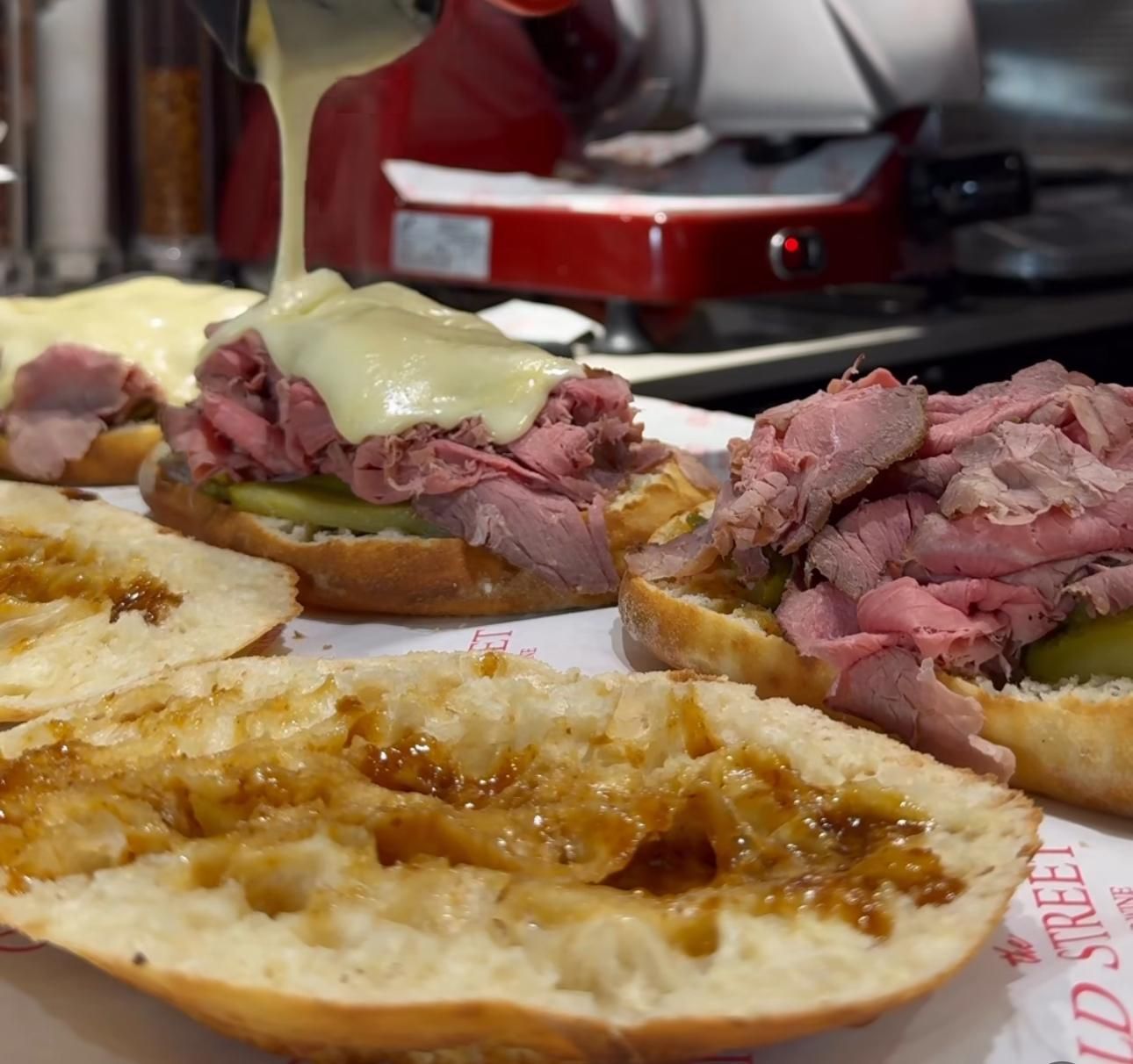 In una cucina di ristorante, una salsa al formaggio calda viene versata su roast beef e sottaceti serviti su panini tostati.