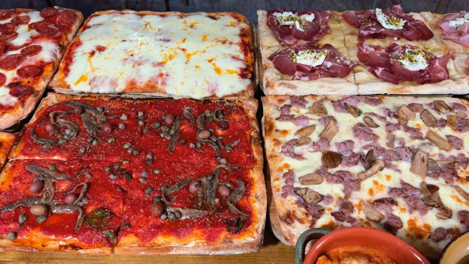Una varietà di pizze rettangolari con diversi condimenti, tra cui salame piccante, formaggio, salumi, olive e funghi.