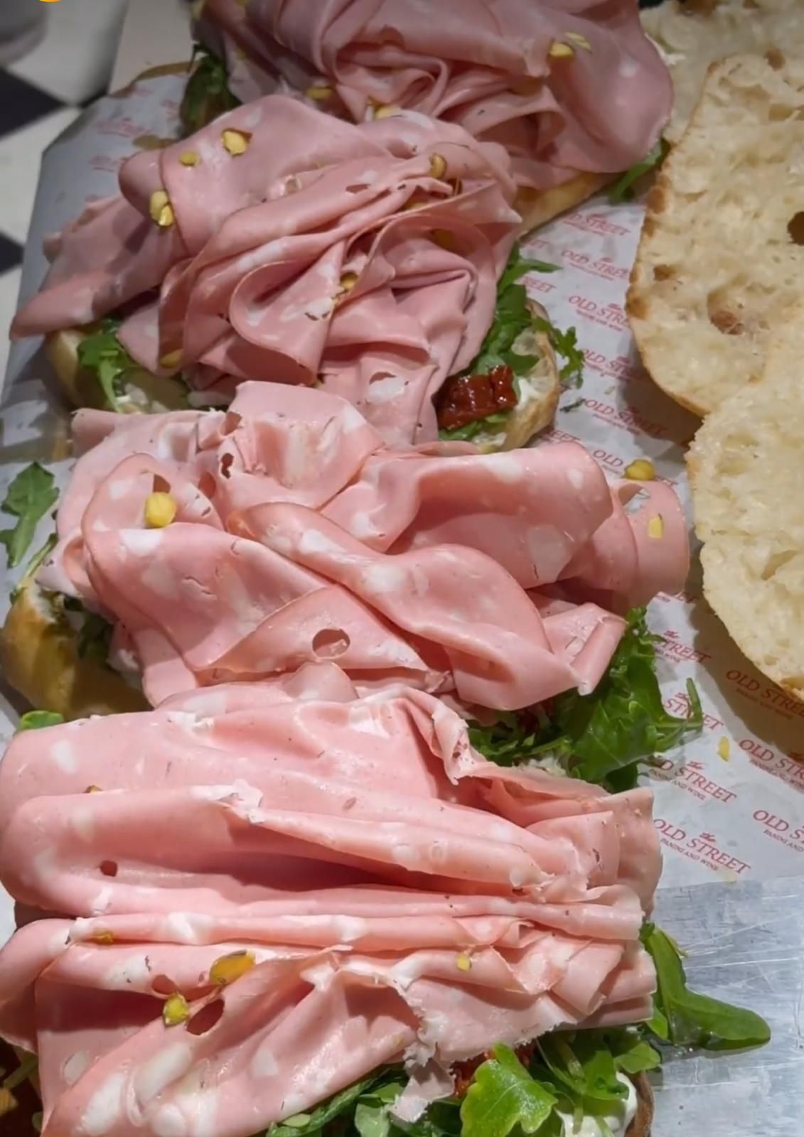 Primo piano di diversi sandwich aperti, farciti con fette di mortadella piegate, rucola verde e noci.
