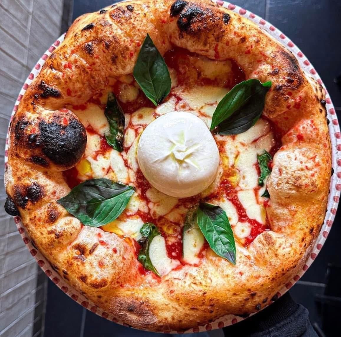 Una pizza in stile napoletano con salsa di pomodoro, formaggio fuso, foglie di basilico fresco e una grande palla di burrata al centro.