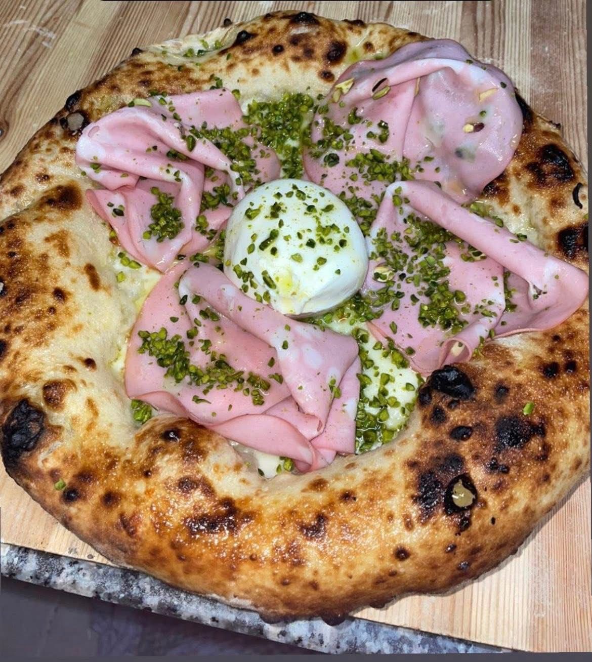 Una pizza gourmet condita con mortadella ripiegata, una palla centrale di burrata e una generosa spolverata di pistacchi tritati.