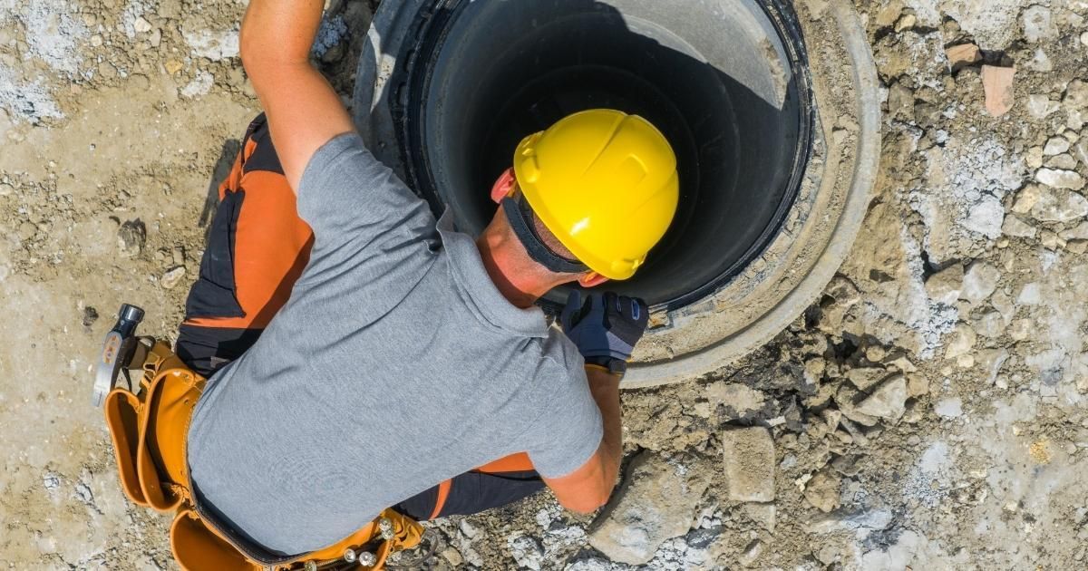 Worker in yellow hard hat entering a large circular pipe opening at a construction site
