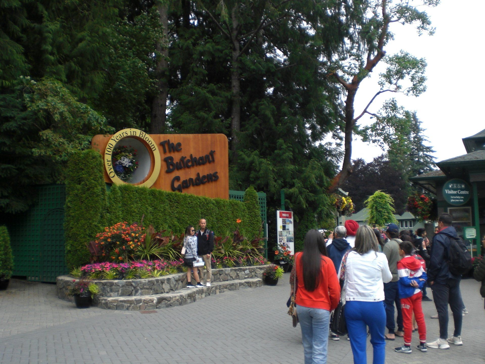 Entrance sign to The Butchart Gardens, with people walking around and lush greenery.
