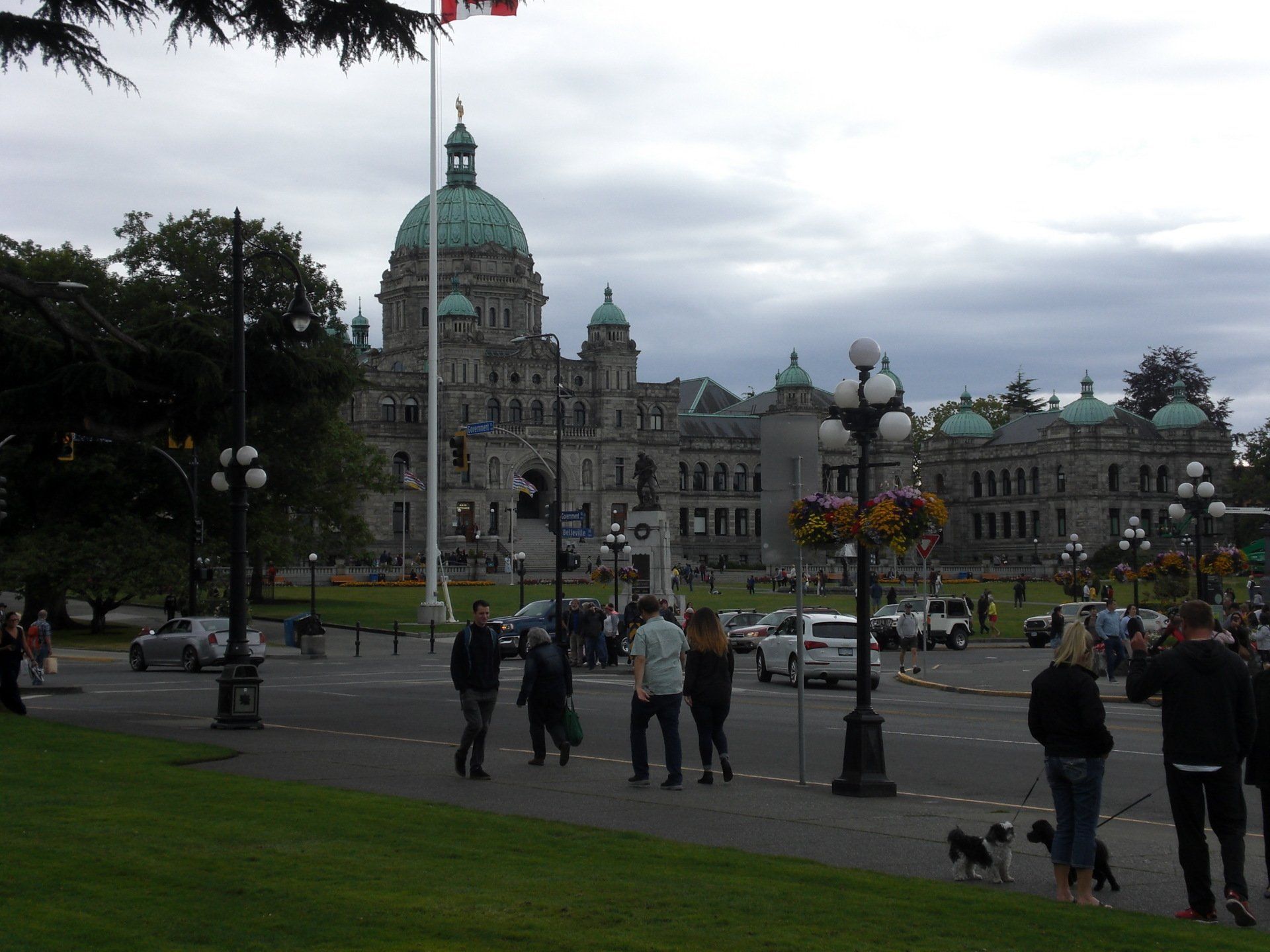 Parliament Buildings, Victoria, BC, with people walking on grass and a cloudy sky overhead.