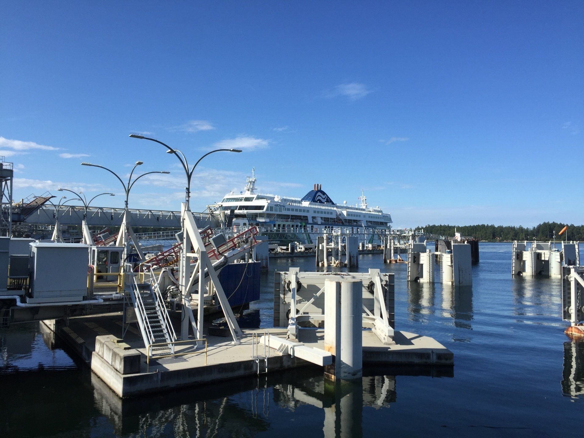 Dock with a large cruise ship, people boarding. Blue sky, water, and concrete docks.