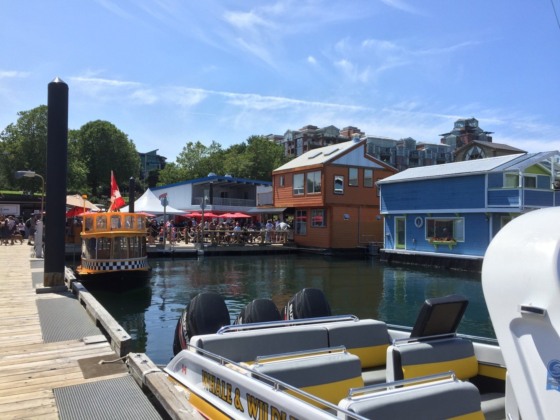 Boats docked at a pier with colorful floating homes and buildings, sunny day.