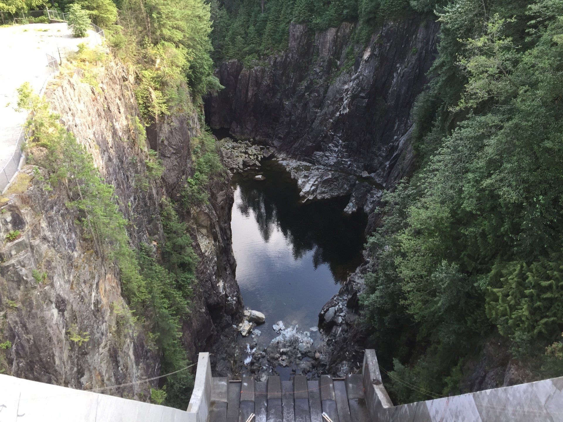 View from a wooden structure into a deep gorge with still water and rocky sides, surrounded by trees.