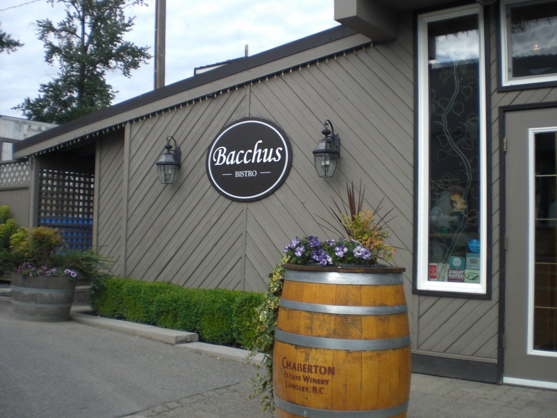 Bacchus restaurant exterior with sign, barrel planter, and diagonal wood siding.