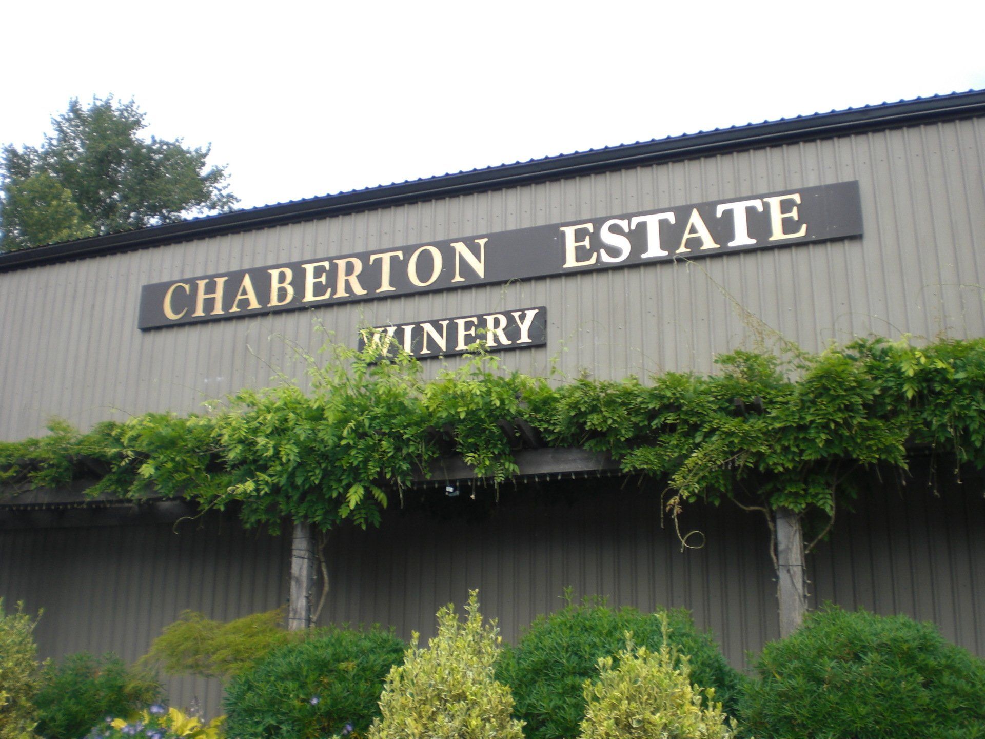 Chaberton Estate Winery building with a sign, covered with green vines and shrubs.