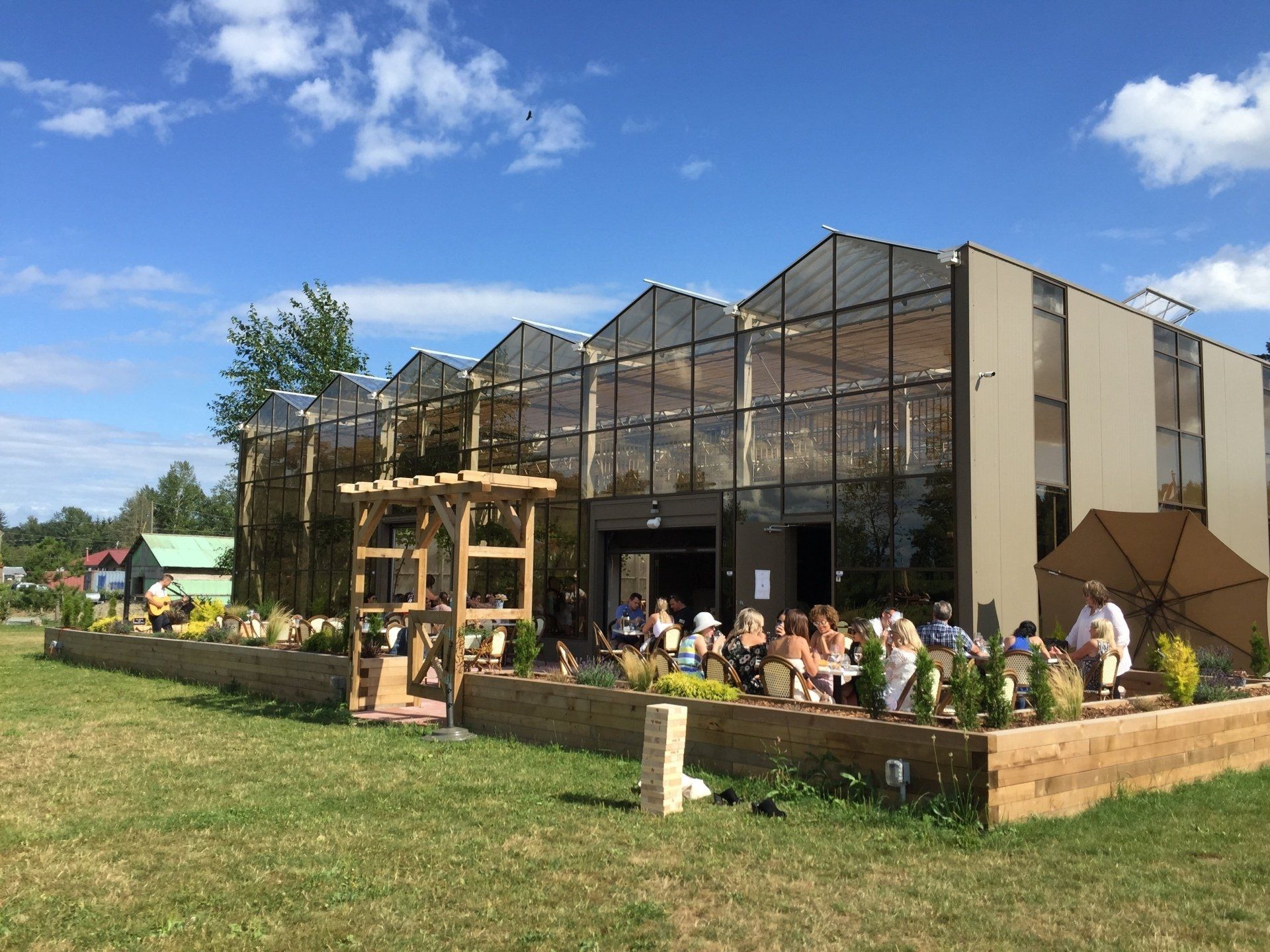 Greenhouse with outdoor seating; people gather on a sunny day.
