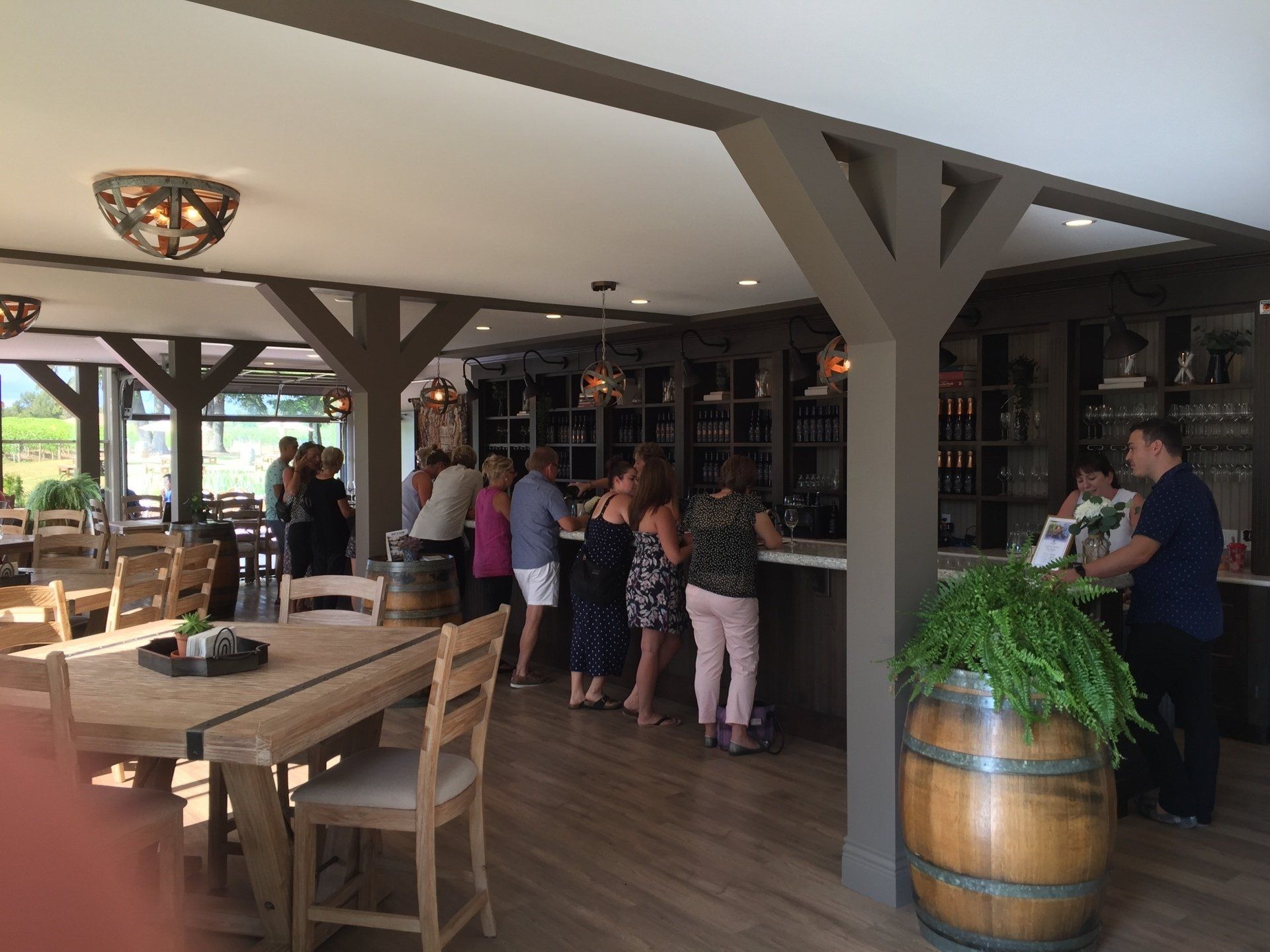 Interior view of a wine tasting room with people at the bar and tables. Wooden accents and barrels.