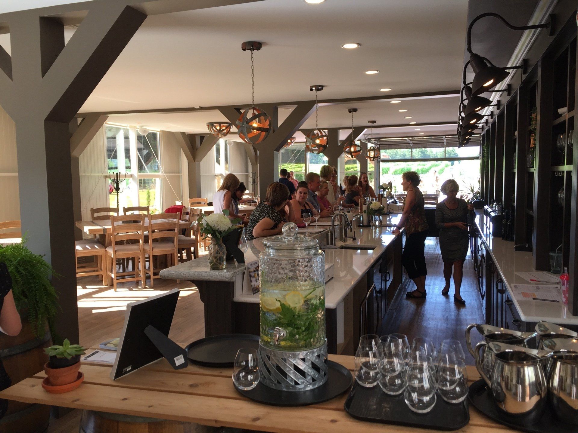 People at a bar, with drinks and glasses. Bright interior, wood and stone features, window in the background.
