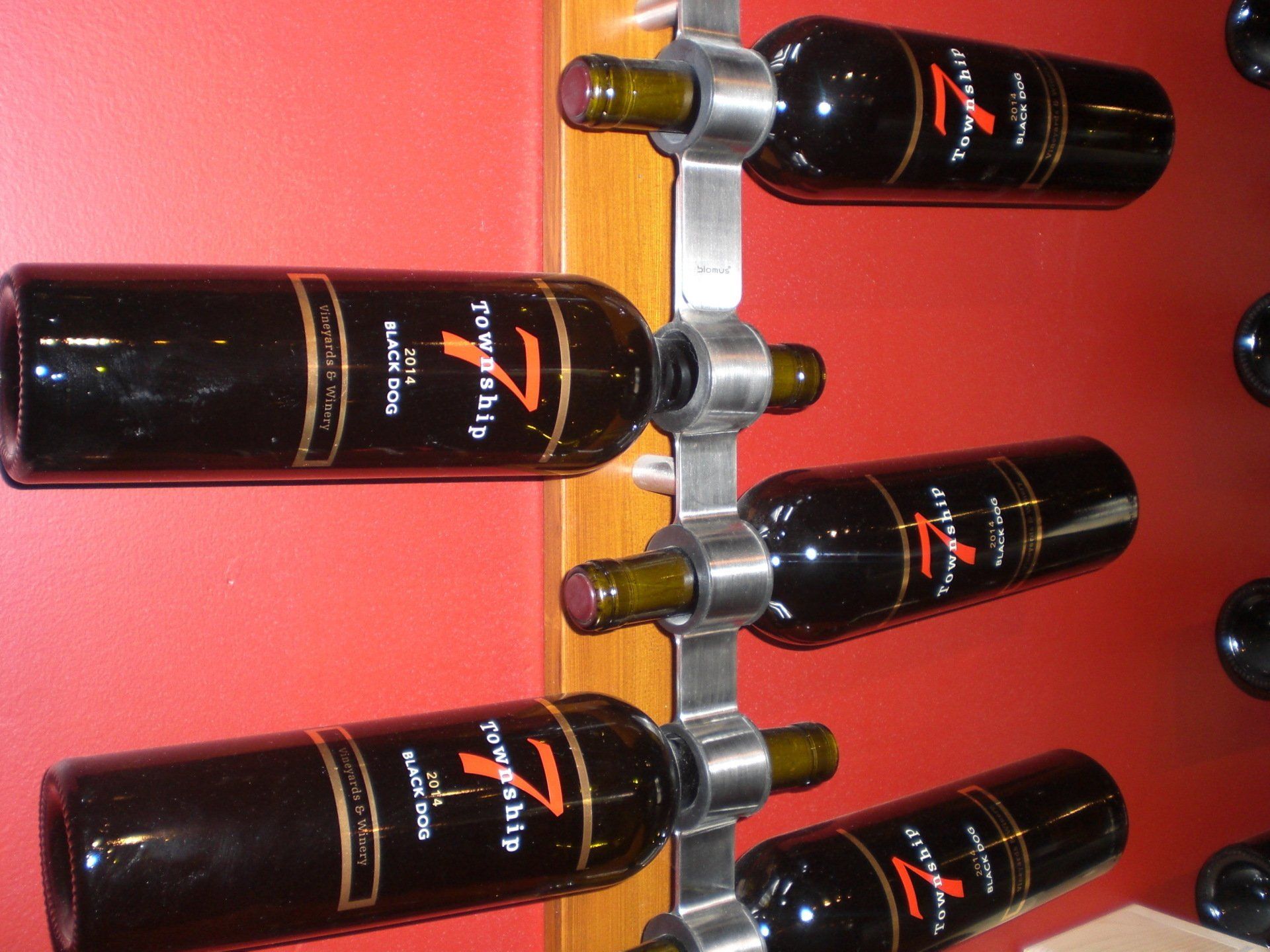 Wine bottles in a metal rack on a red wall.