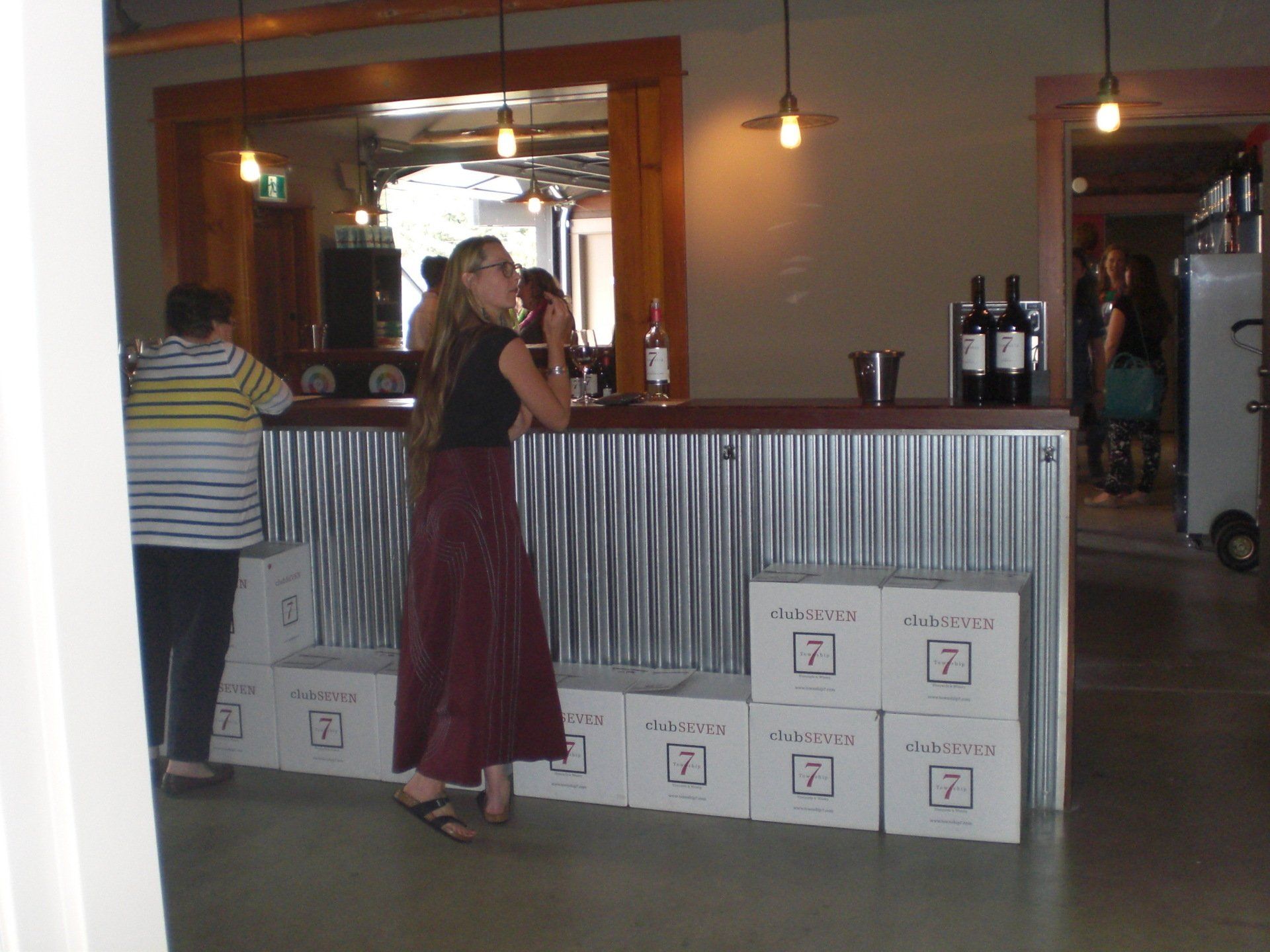 A woman leans on a corrugated metal bar, next to boxes with a 