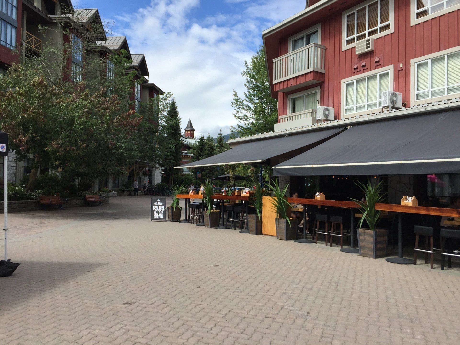 Exterior view of a restaurant with outdoor seating. Red building with black awnings and a brick-paved walkway.