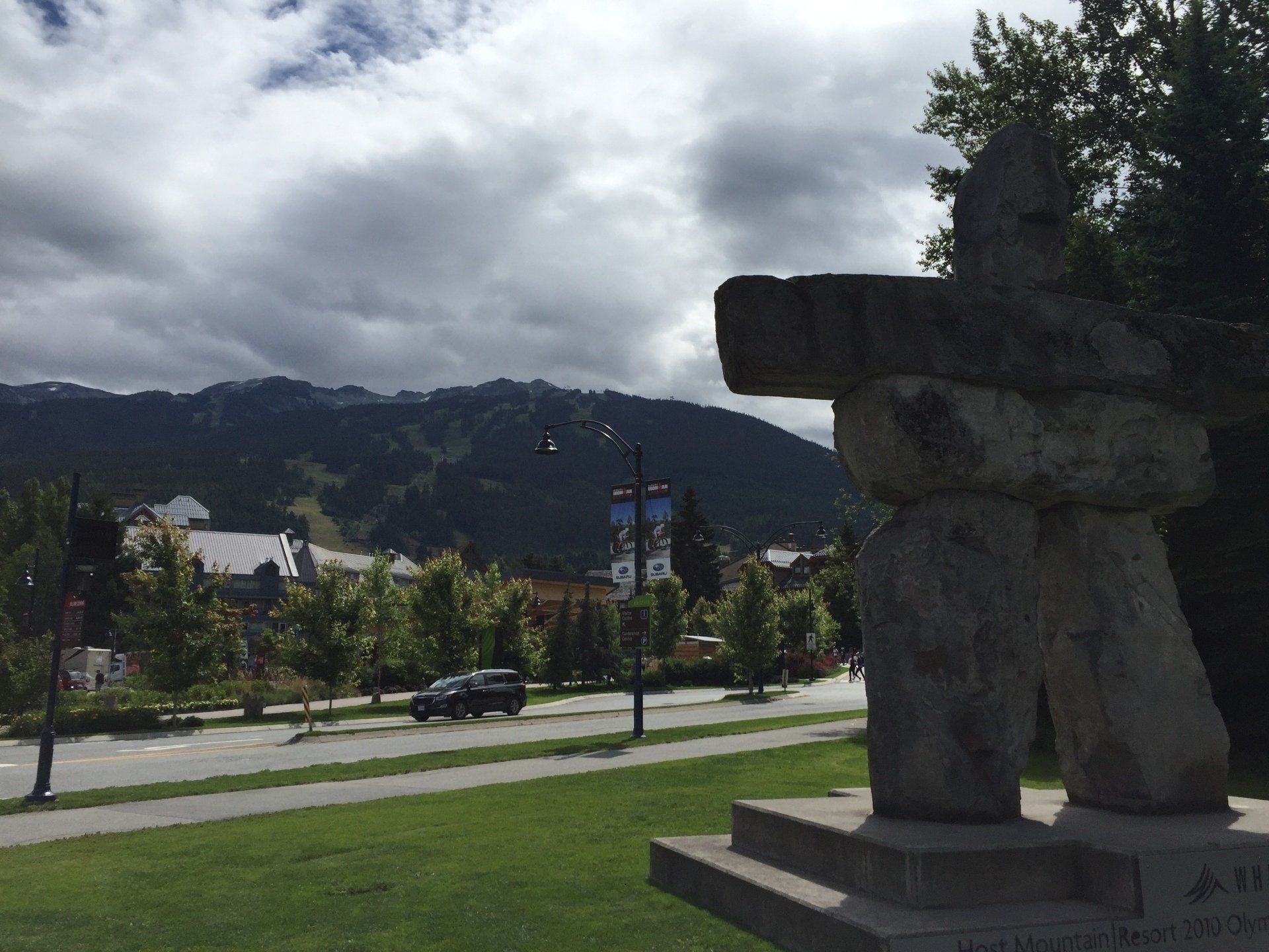 Stone Inukshuk statue with a mountain backdrop and cloudy sky.