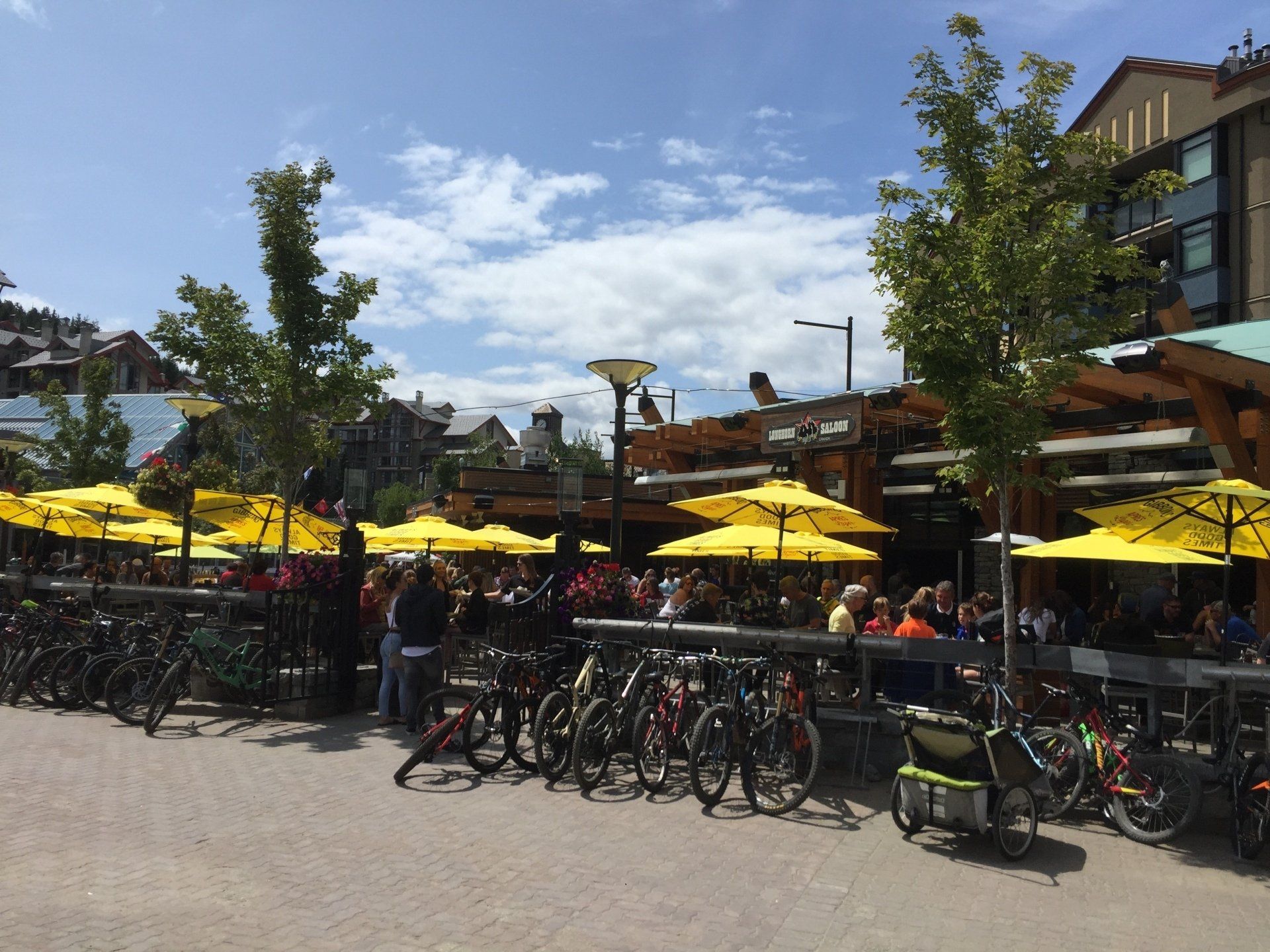 Outdoor restaurant with yellow umbrellas, bikes, and people on a sunny day.