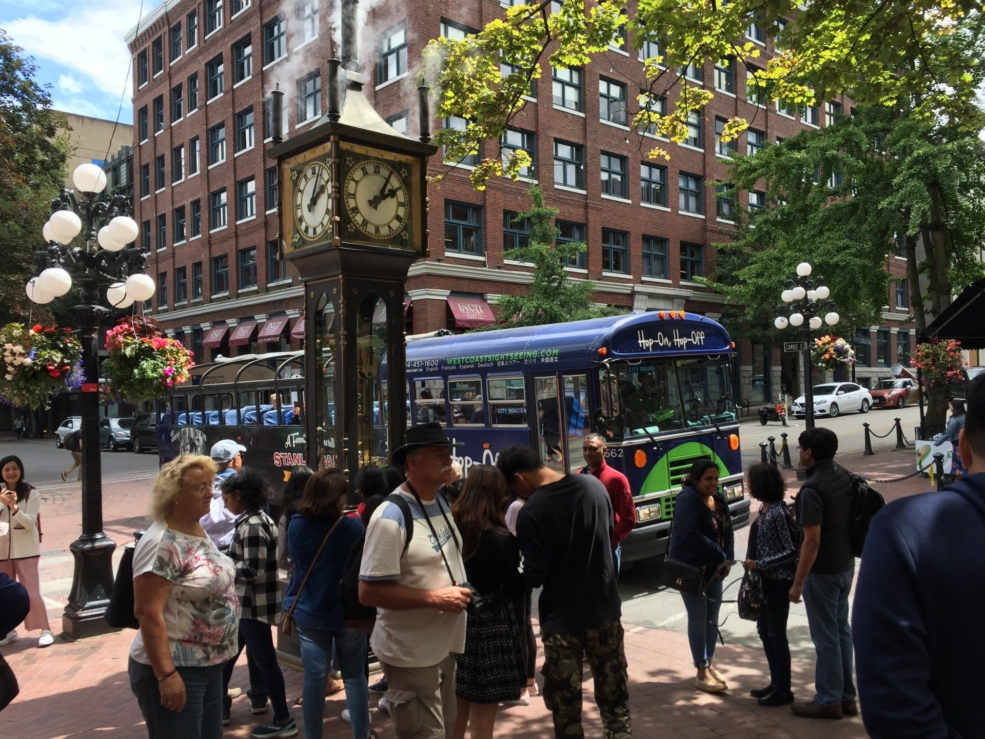 People near a clock tower and bus in Gastown, Vancouver. Tourists are standing in the street.